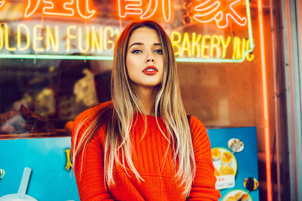 woman in red sweater stands in front of a Chinese bakery neon sign