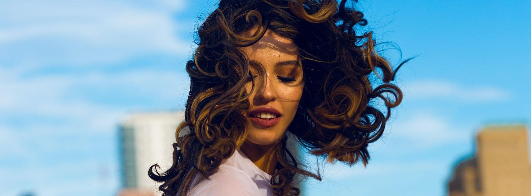 curly haired woman standing outside with windblown hair