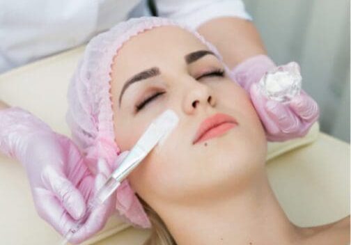 Woman receiving facial treatment with brush.